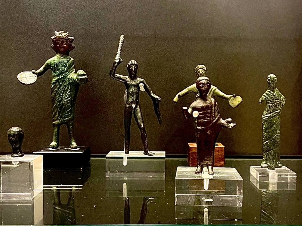 Small bronze statues of Etruscans from Chiusi, showing men, women, and children in daily activities, highlighting clothing, gestures, and social life in ancient Etruria.